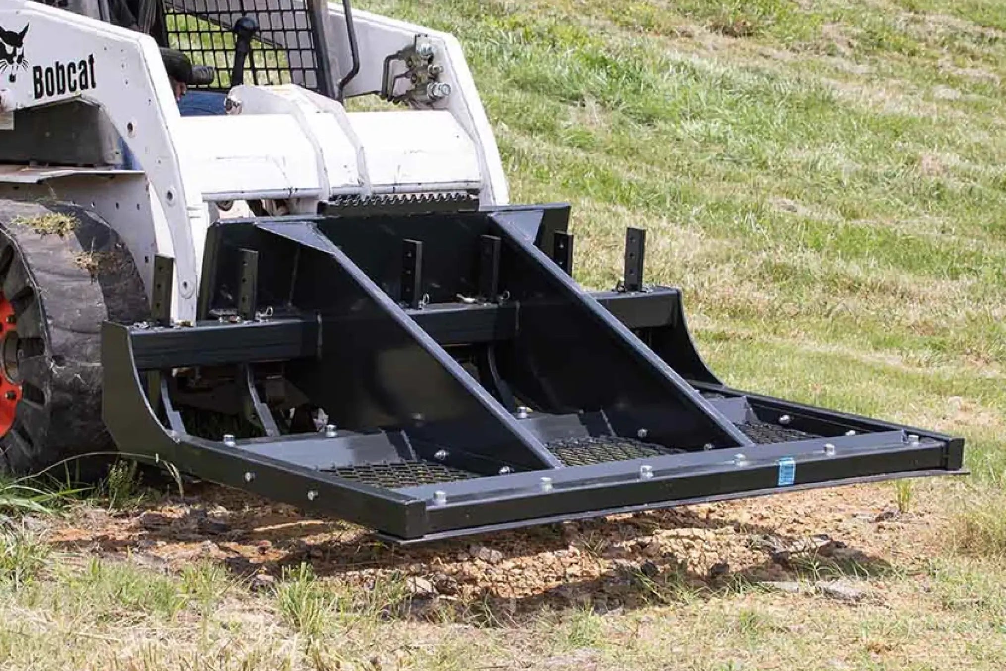 Black steel box blade attachment on Bobcat skid steer for land grading and leveling.