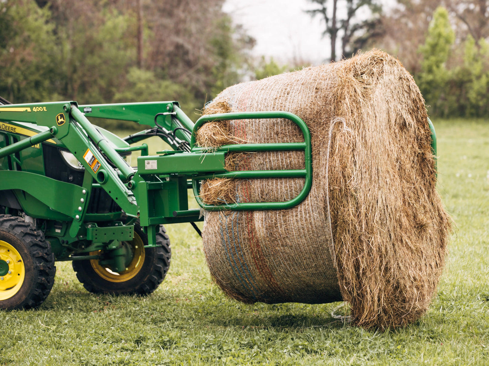 Green tractor with a front grapple lifting a large round hay bale